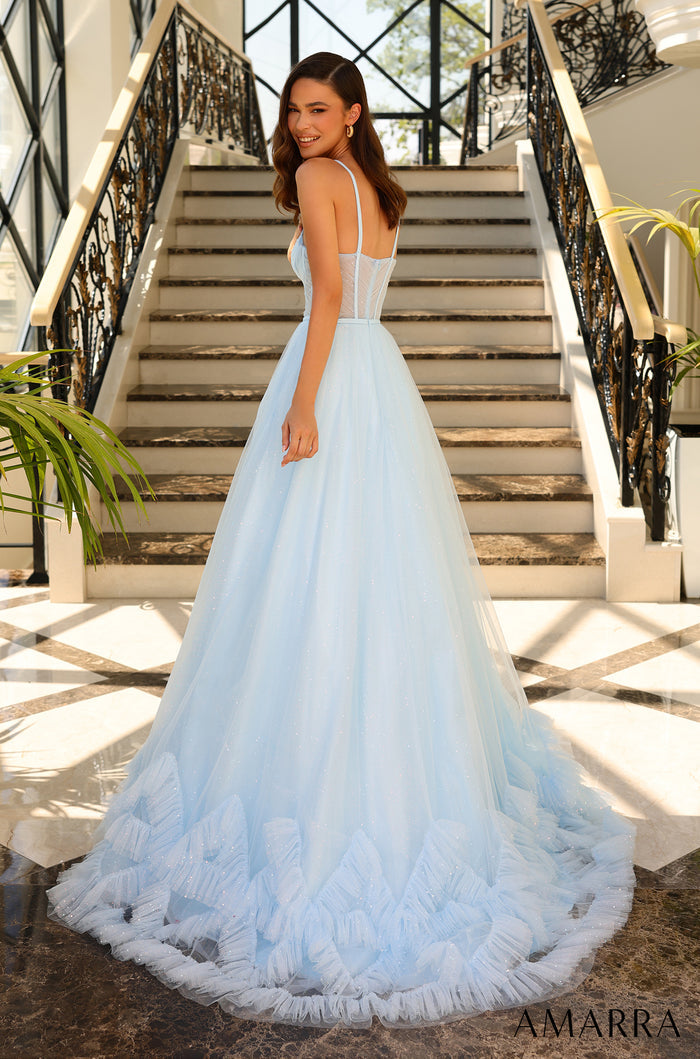 A woman in a light blue ball gown with a ruffled skirt stands on marble stairs with ornate railings.