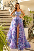 A woman wears a dramatic Lilac/Multi ruffled ball gown with a high slit on an elegant staircase.