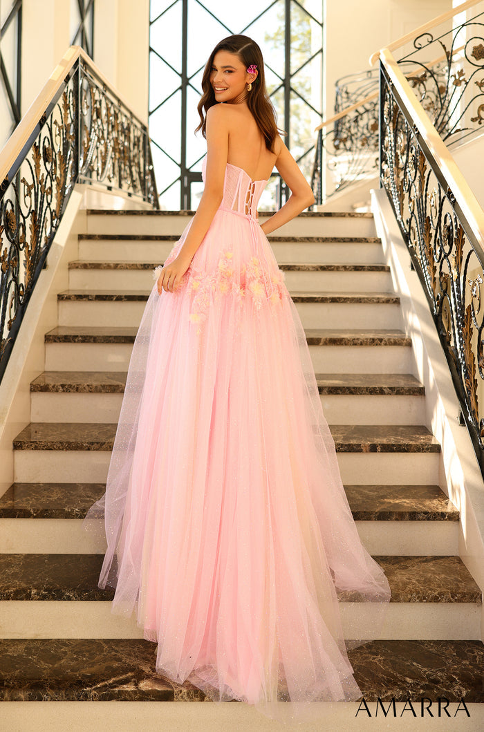 A person wears a strapless pink tulle ball gown while standing on marble stairs with ornate iron railings.