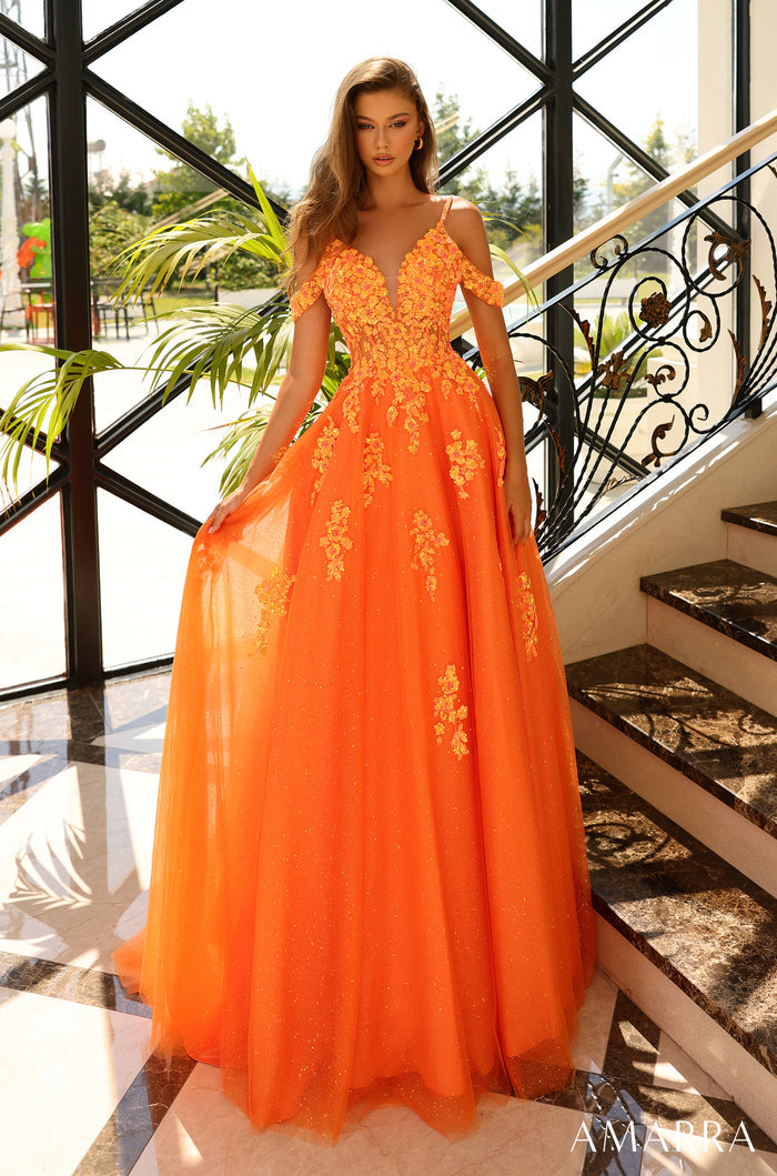 A model wears a floor-length, neon orange ball gown with floral embellishments and cold-shoulder straps.