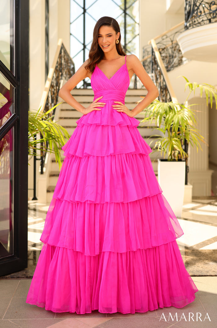 A woman models a hot pink tiered ball gown with spaghetti straps in an elegant indoor setting.