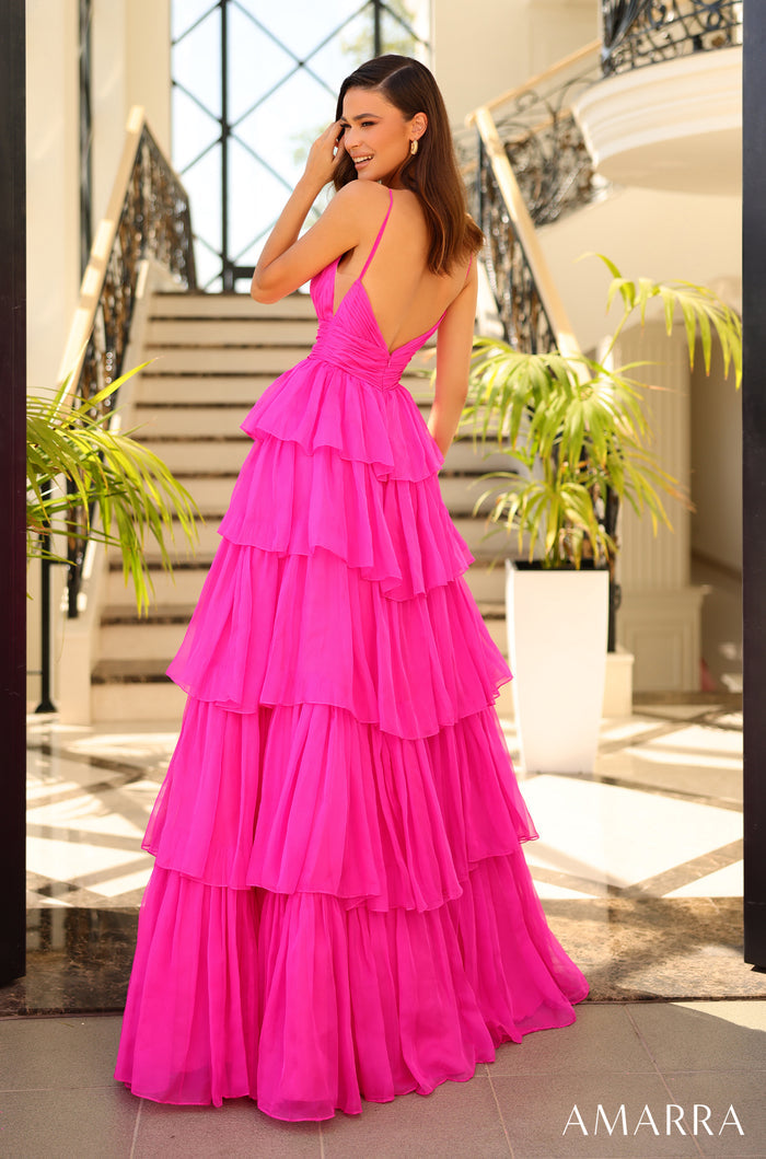 A woman in a vibrant pink tiered gown with a low back stands on a tiled floor near a staircase.