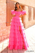 A smiling woman wears a vibrant pink tiered tulle gown with off-shoulder ruffles against a stone wall backdrop.