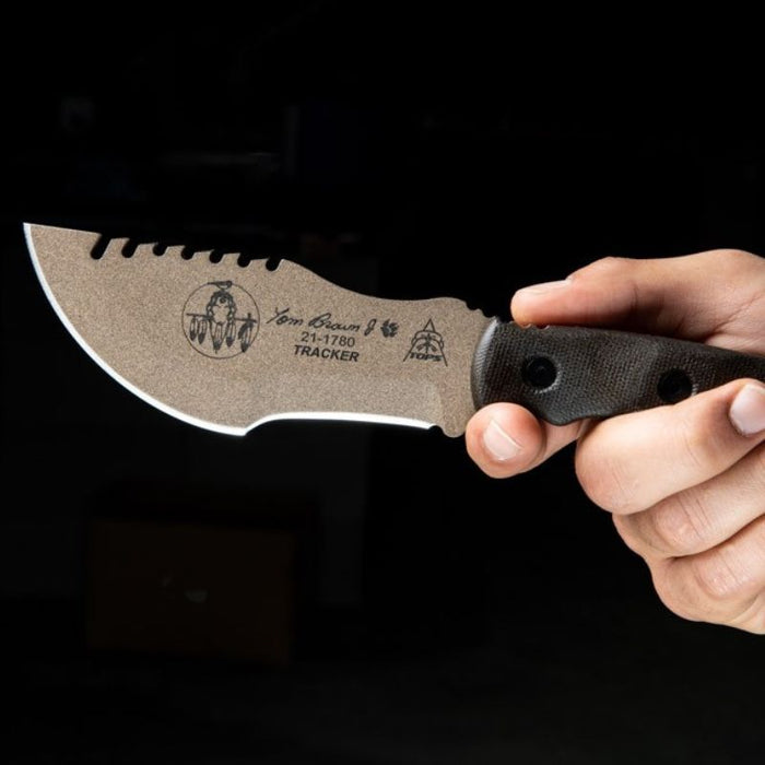 Hand holding a knife with a brown handle and textured blade against a dark background