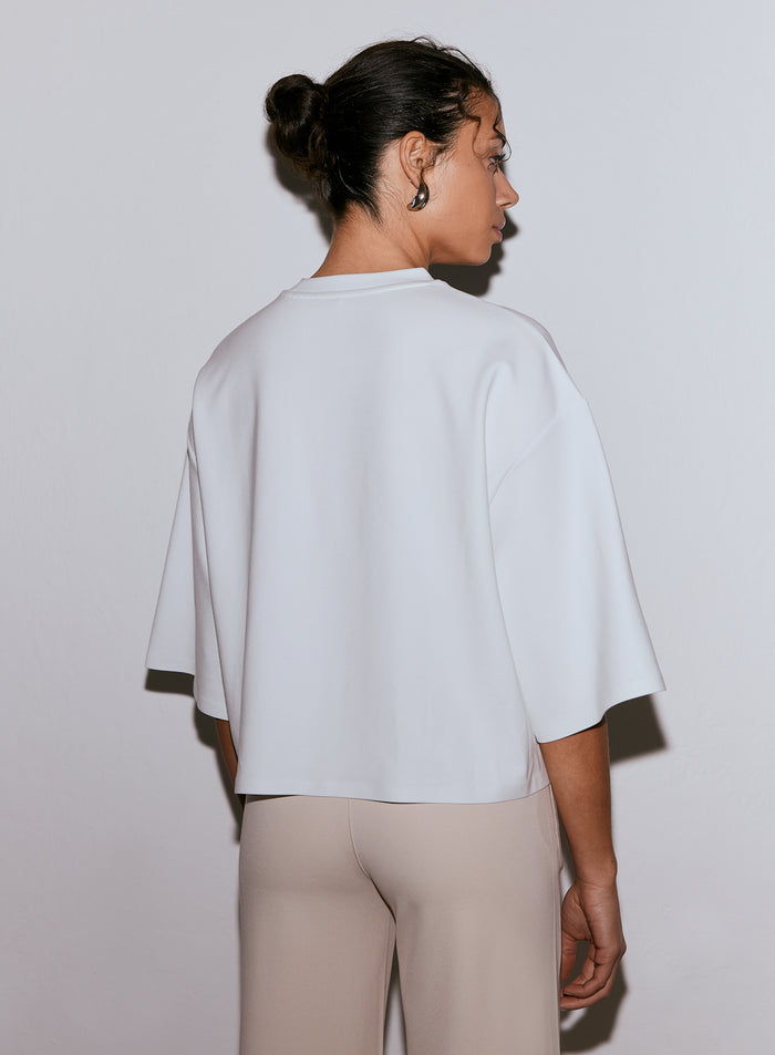 Nainen takaapäin yllään valkoinen Luxe Boxy Short Sleeve -paita ja vaaleat housut. [M-170cm]