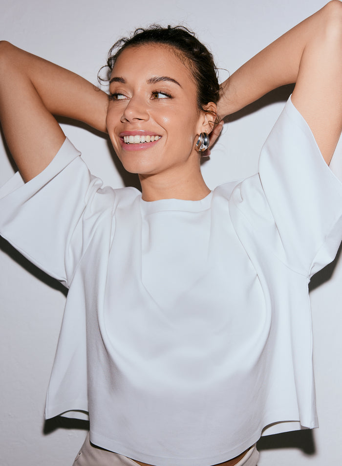 Hymyilevä malli yllään valkoinen Luxe Boxy Short Sleeve -toppi, kädet pään takana [M-170CM]