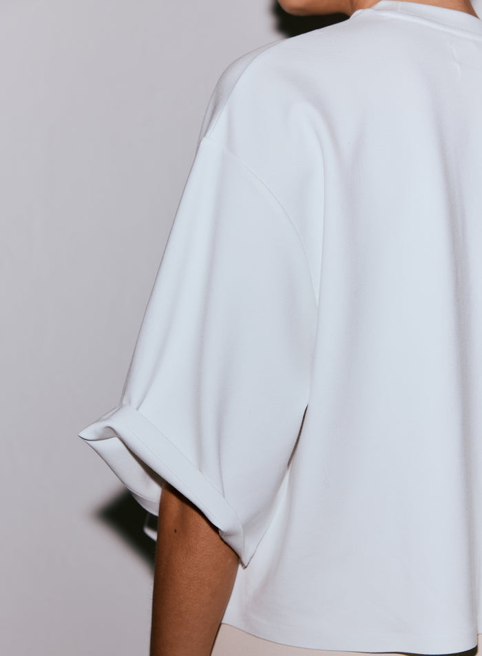 Lähikuva henkilön yllä olevan valkoisen Luxe Boxy Short Sleeve -topin selästä ja kääritystä hihasta. [M-170cm]