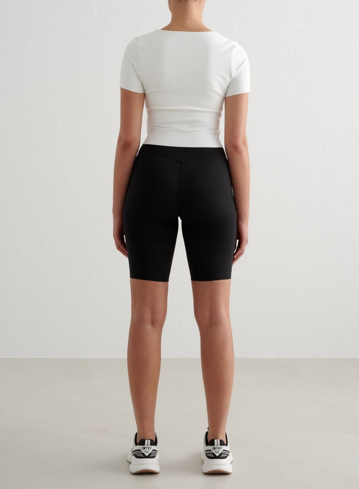 Valkoinen Sense Short Sleeve Bralette second skin -tuntumalla, kuvattuna takaa mustien biker-shortsien kanssa.
